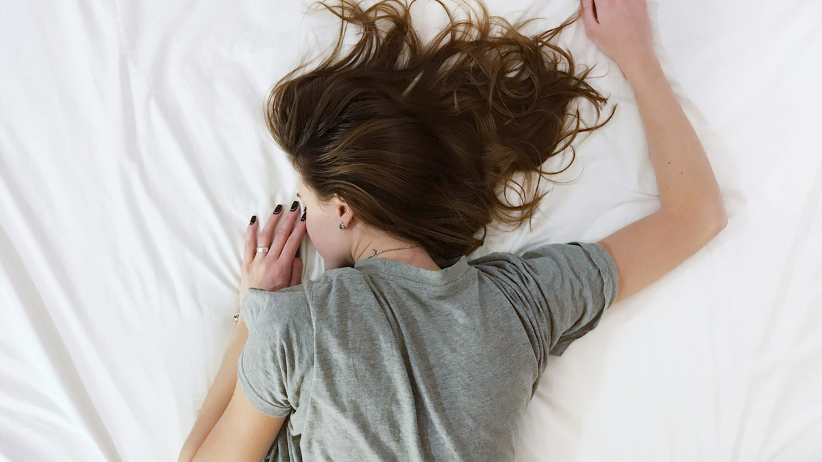 Frau mit langen Haaren liegt entspannt auf einem hellen Bett