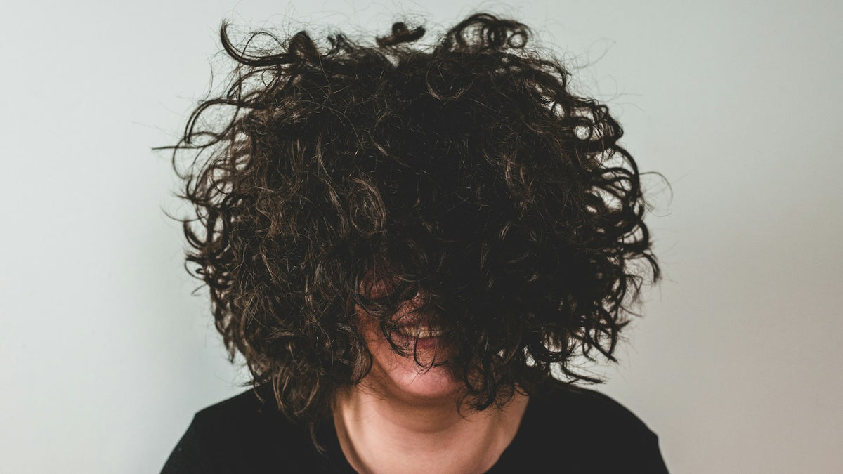 Person mit dichten dunklen Locken, die das Gesicht teilweise verdecken