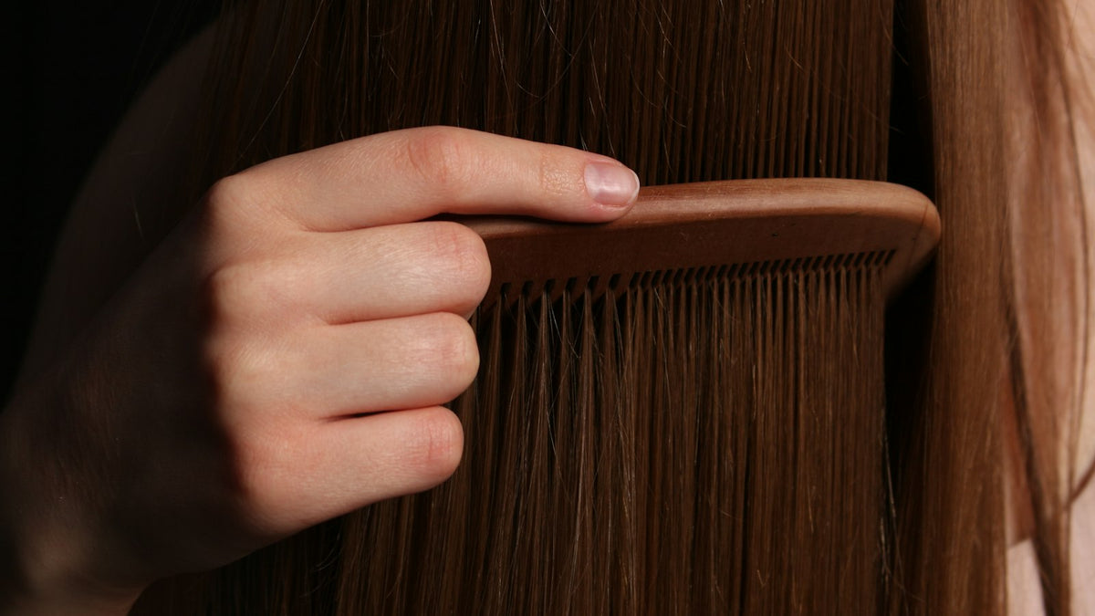 Hand bürstet langes, braunes Haar durch
