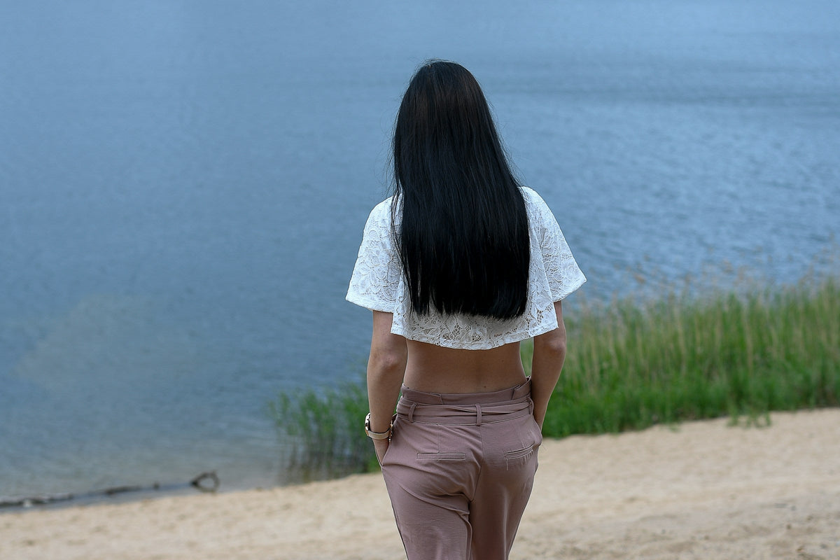 Frau mit langen braunen Haaren von hinten am Sandstrand – Haare nach dem Sommer