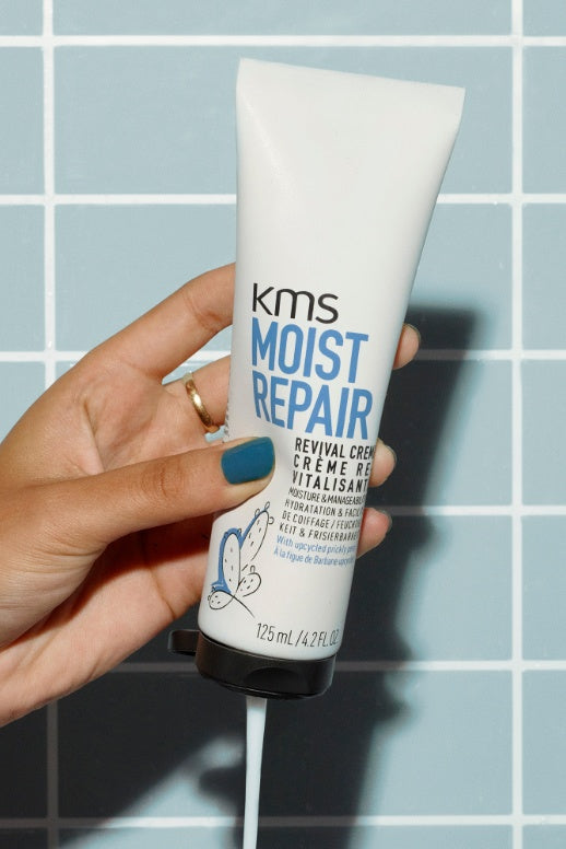 KMS Moistrepair Revival Creme, Tube in der Hand vor Fliesenwand