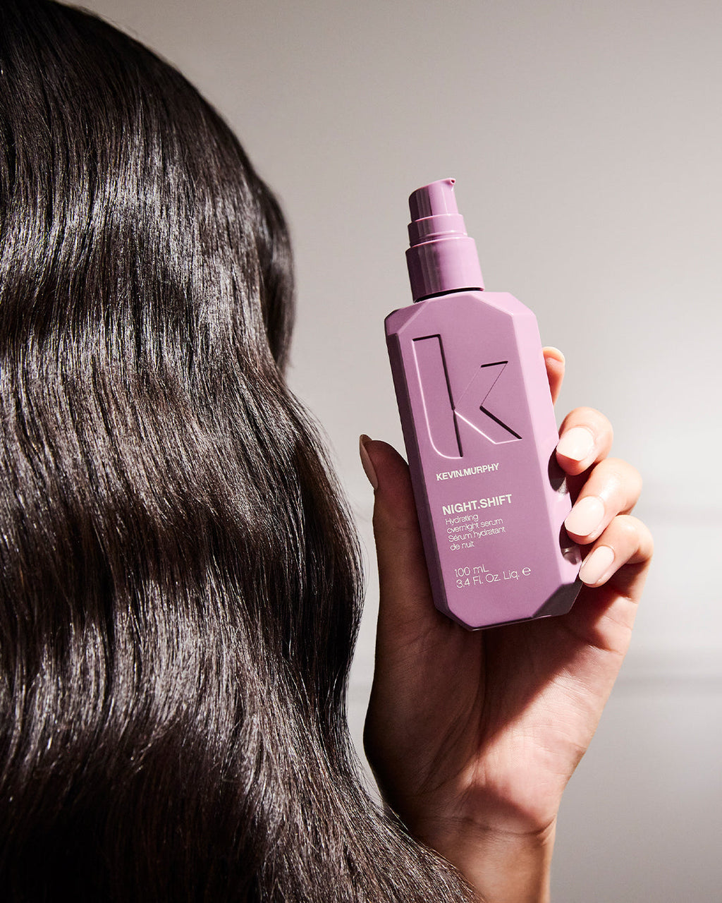 Hand hält die Kevin Murphy Night Shift Flasche vor geglättetem Haar