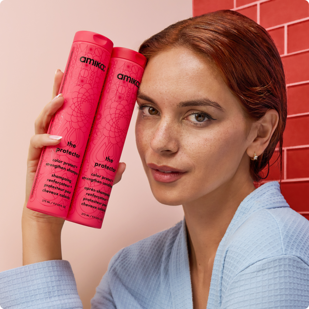 amika Haarpflege – Model mit rotem Haar hält amika Shampoo und Conditioner