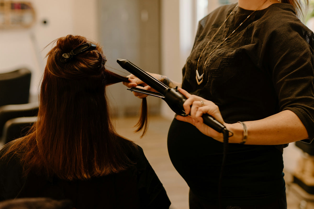 Hitzeschutzspray – Friseurin glättet im Salon eine Haarsträhne mit dem Glätteisen