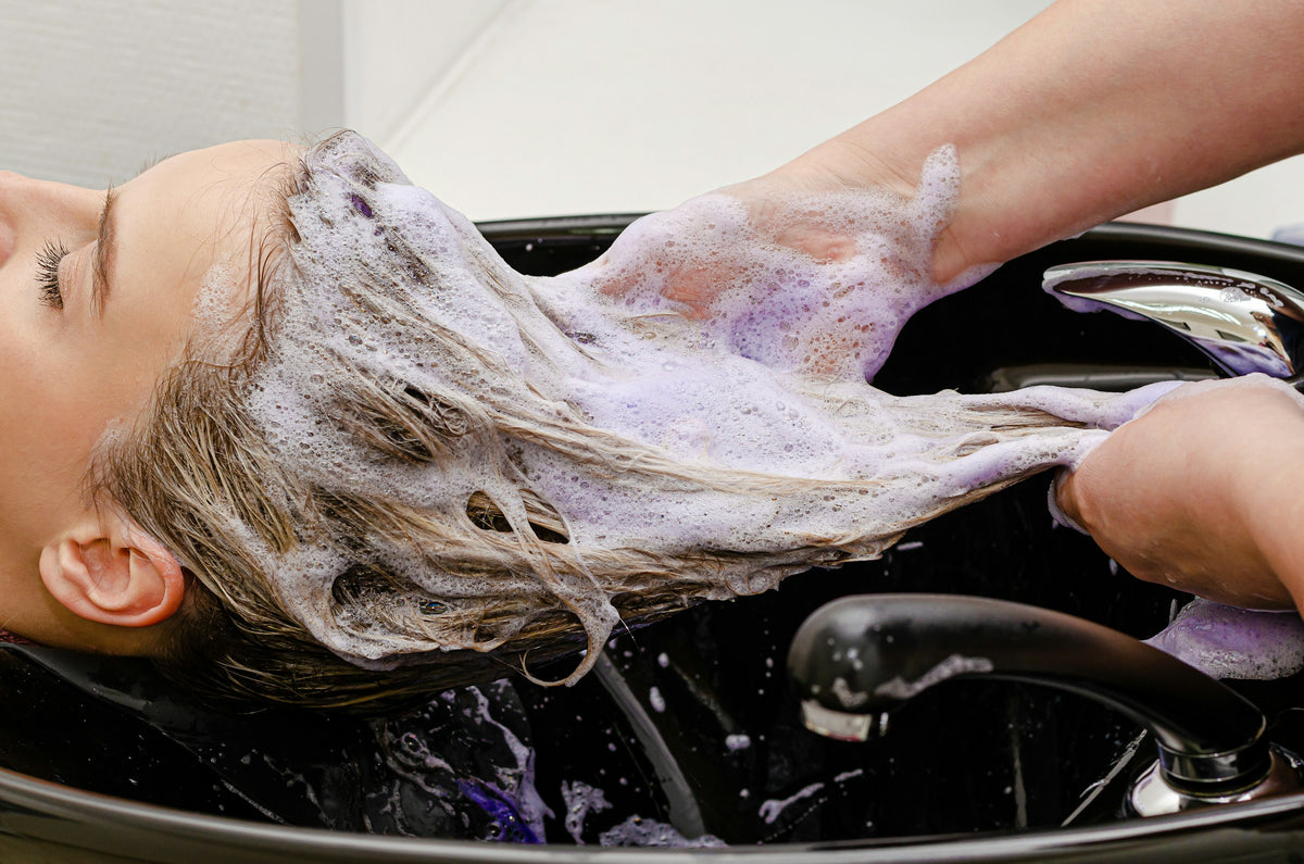 Silbershampoo – blondes Haar wird im Salon mit violettem Schaum gewaschen
